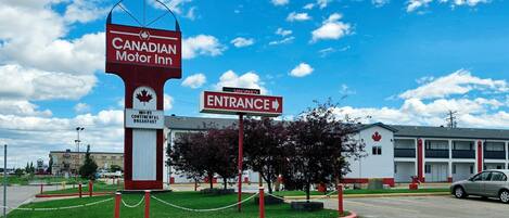 A Canadian Motor Inn with a sign indicating Wi-Fi and continental breakfast, an entrance sign, and a parking lot with a car.