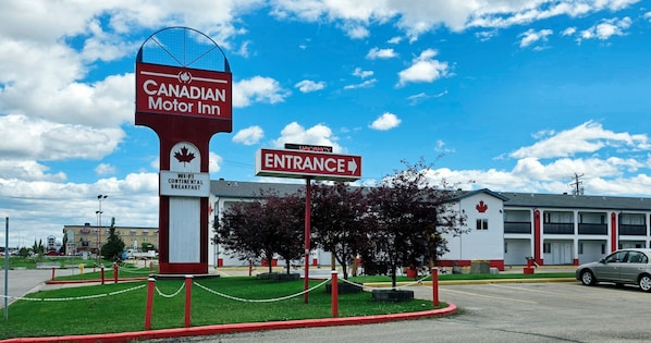 A Canadian Motor Inn with a sign indicating Wi-Fi and continental breakfast, an entrance sign, and a parking lot with a car.