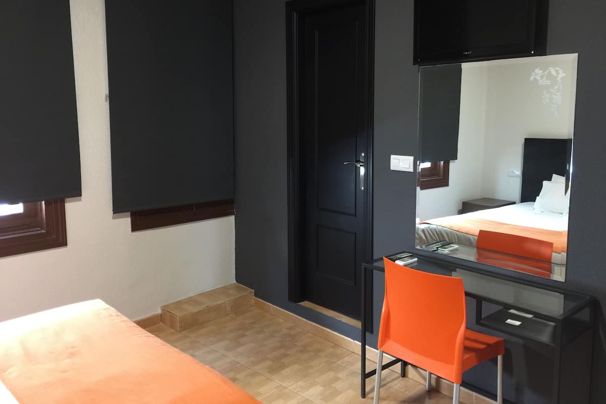 Una habitación con una cama, un escritorio, una silla, una puerta y un espejo.