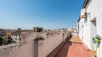 Una terraza en la azotea con vistas a un paisaje urbano, un edificio blanco con una manguera y una cubierta de madera.