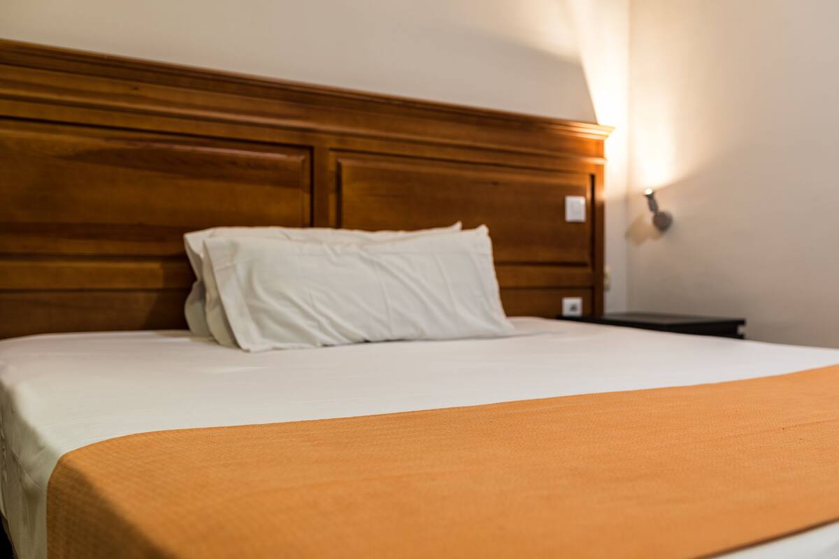 Una cama bien hecha con cabecera de madera, ropa de cama blanca y una manta marrón.