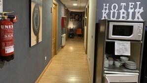 Corredor de hotel com piso de madeira, um extintor, uma porta e uma área de kitchenette com micro-ondas e máquina de café.