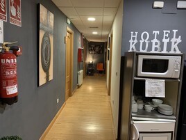 Pasillo de hotel con suelo de madera, extintor, una puerta y una zona de kitchenette con microondas y cafetera.