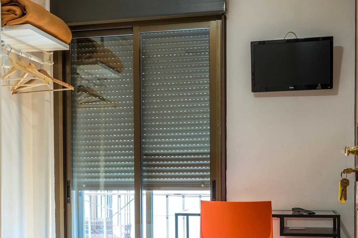 Habitación de hotel con cama, escritorio, silla, televisor y puerta corredera al exterior.