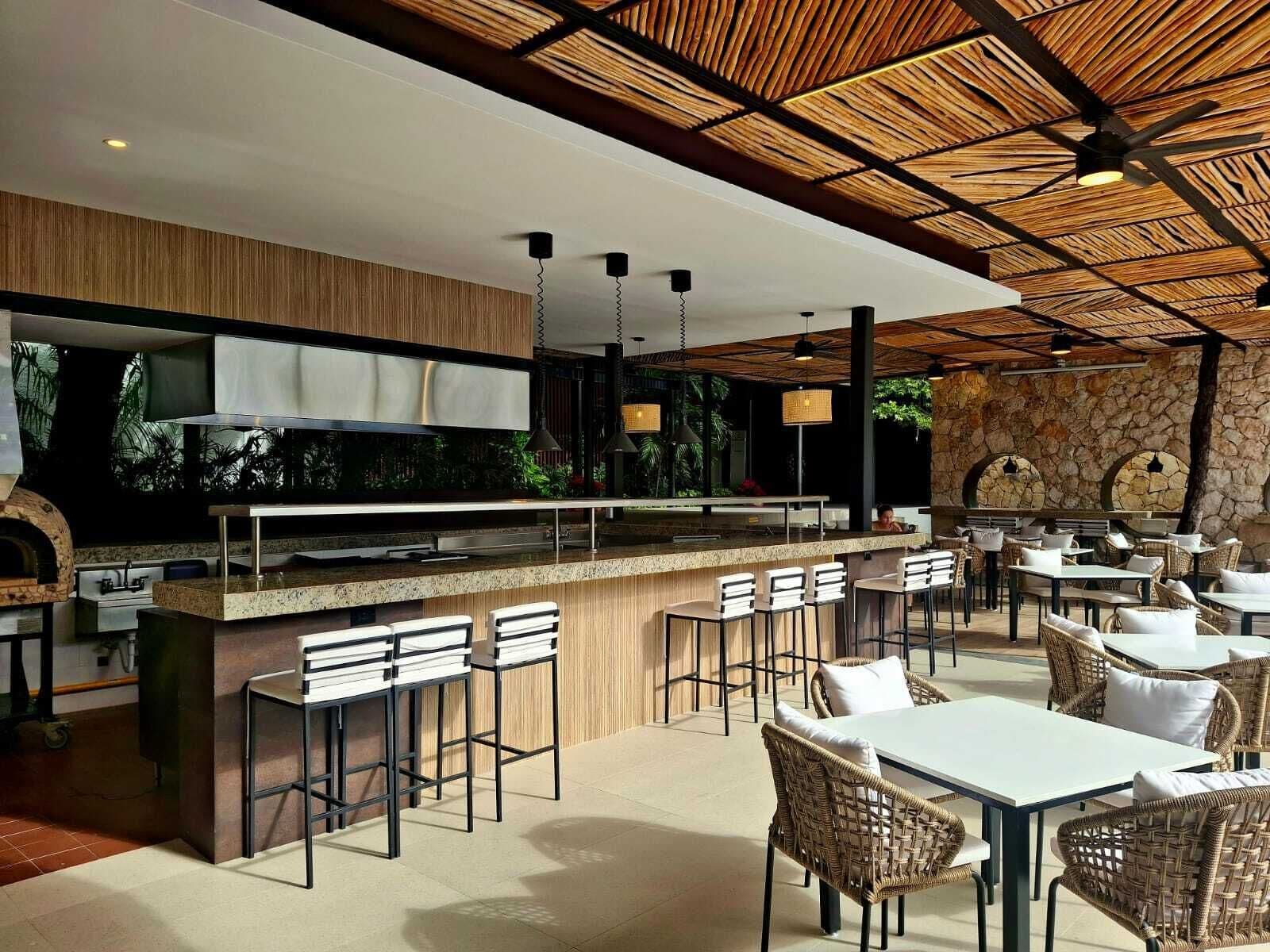 Un área de comedor al aire libre moderna con un muro de piedra, techo de madera y taburetes de bar.