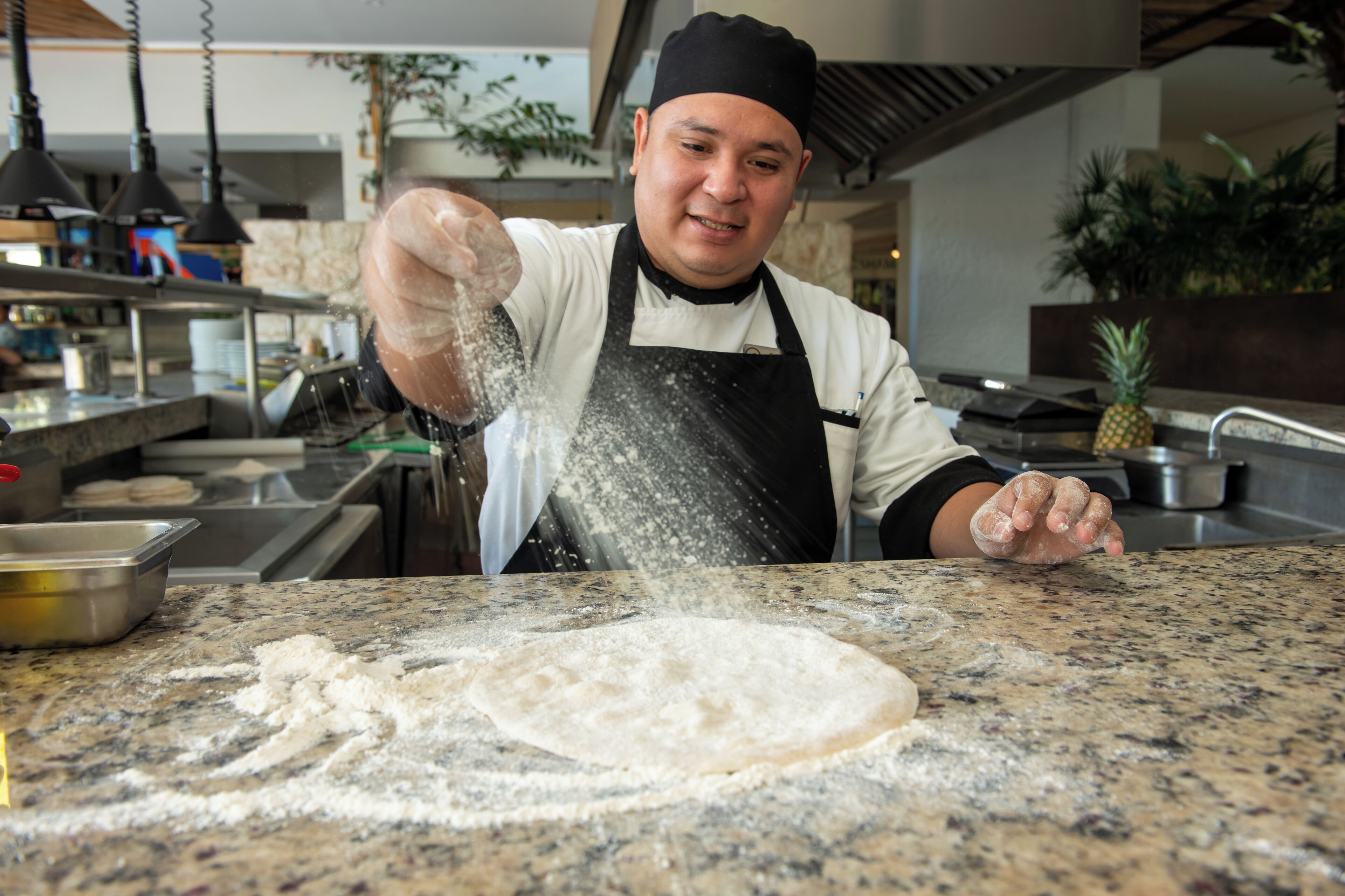 A chef sprinkling flour on a countertop in a kitchen.