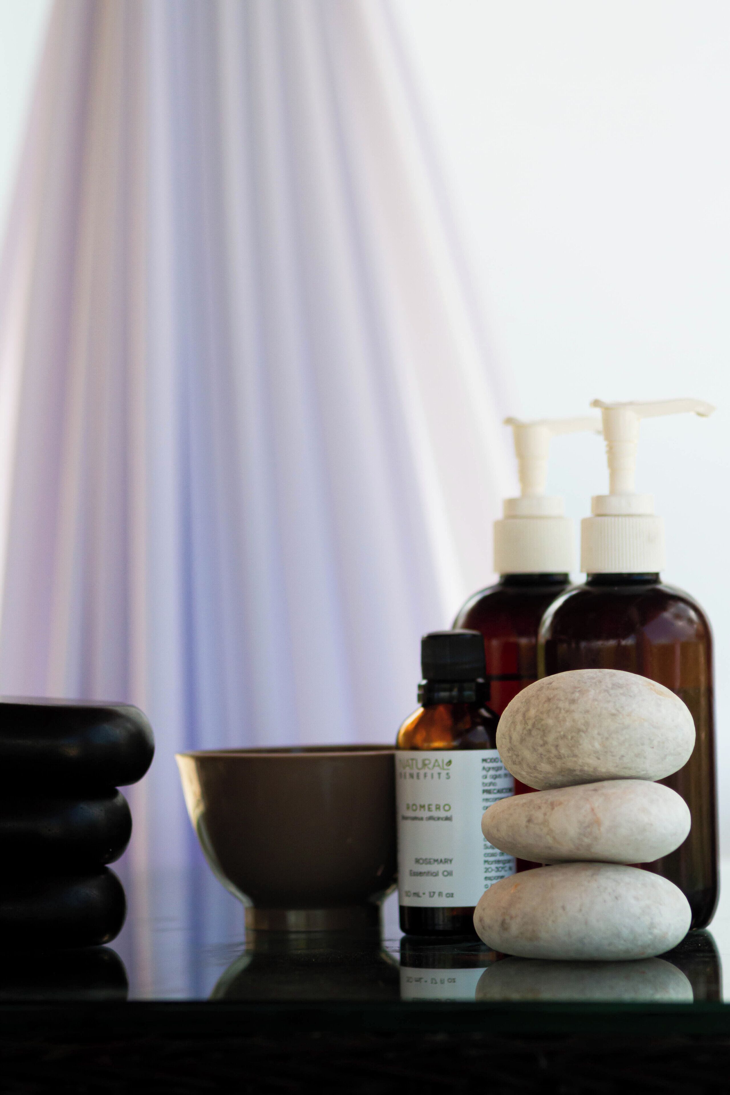 Un meuble-vasque de salle de bain avec un bol, deux flacons d’huiles essentielles et une pile de pierres.