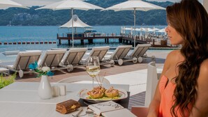 A dining area with a view of the sea, outdoor seating, and a table with a glass of wine and seafood. - B Pichilingue Acapulco (Acapulco)