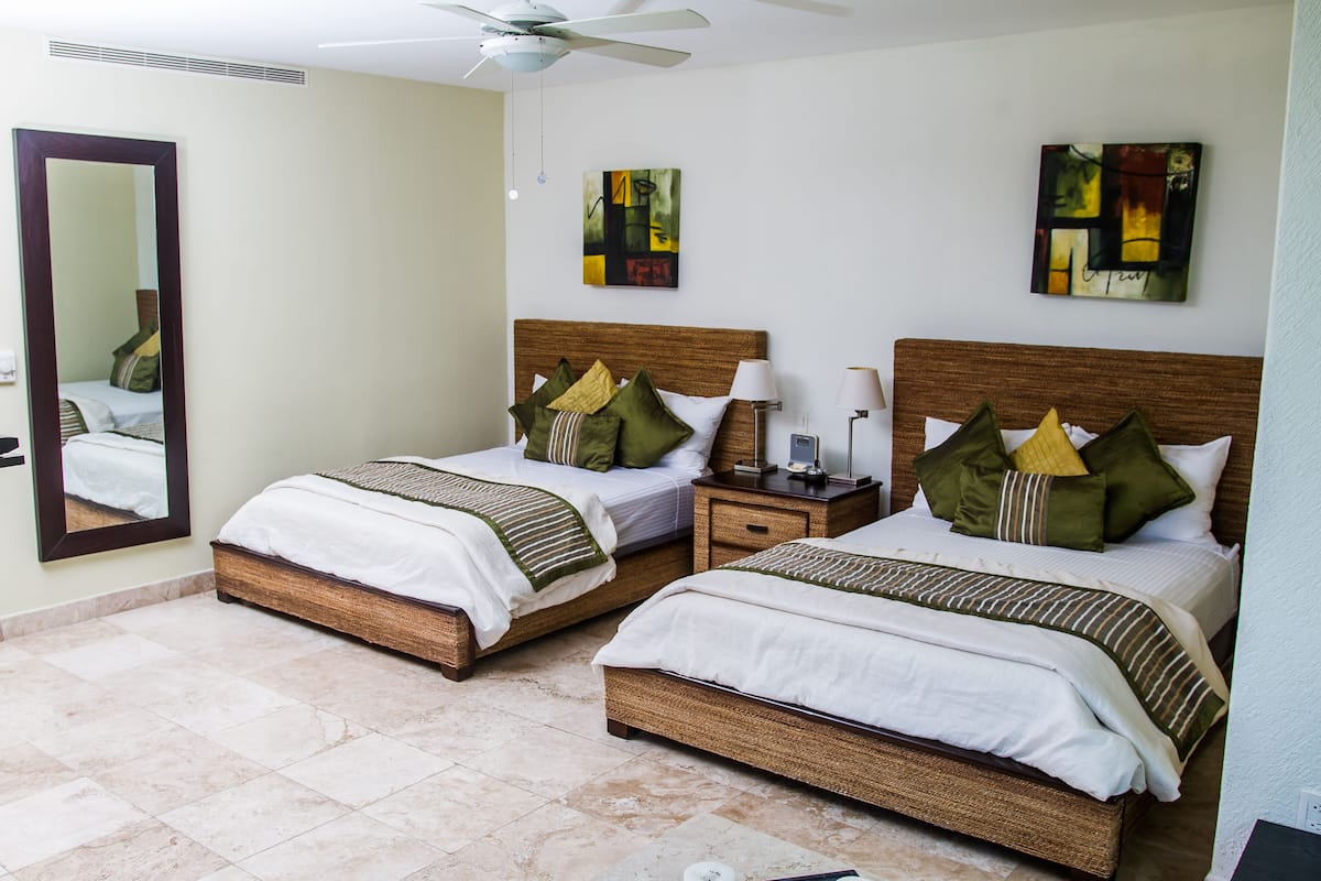 A hotel room with two beds, a ceiling fan, artwork on the walls, and a large mirror.