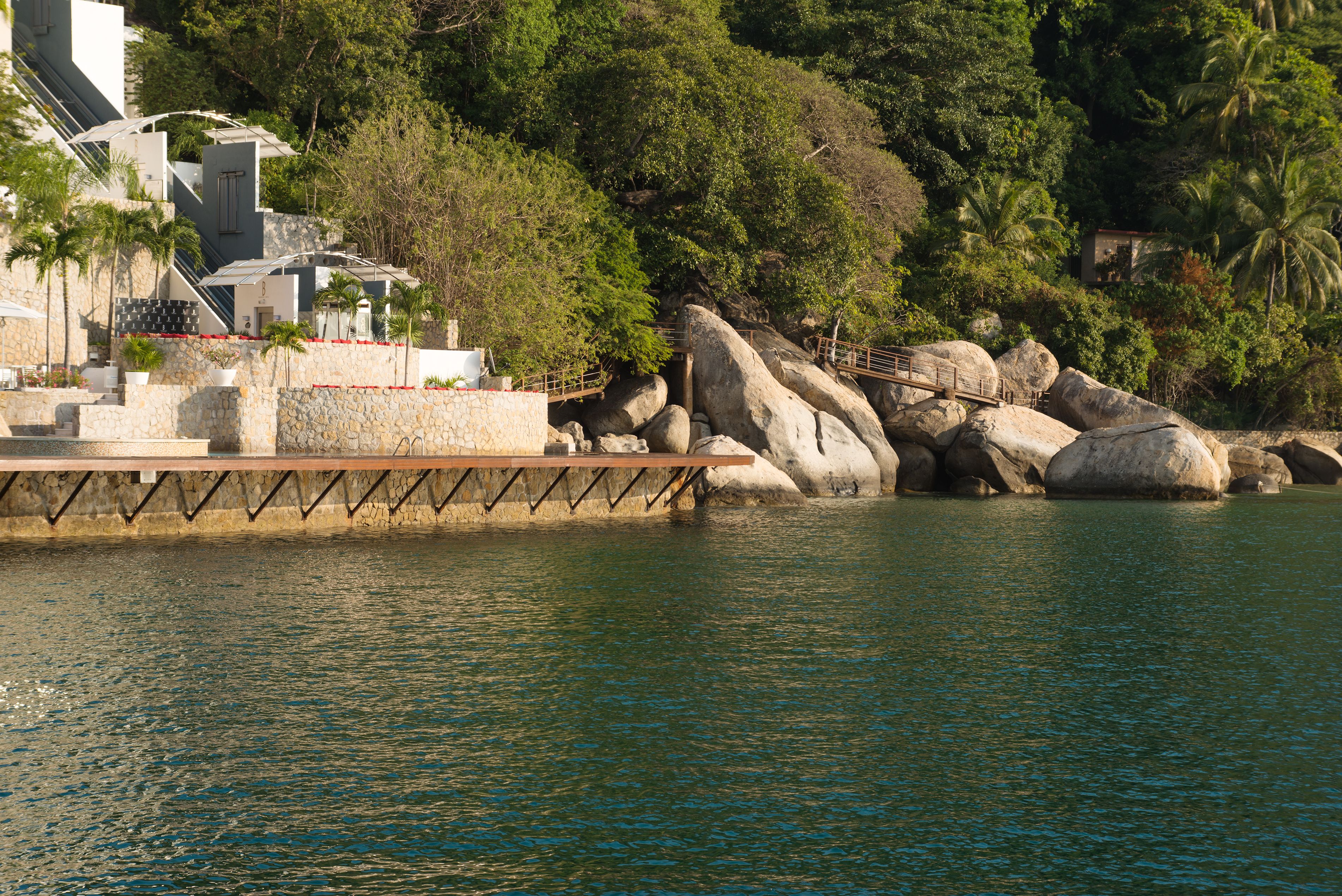 A waterfront hotel with a stone facade, a wooden deck, and large rocks.