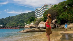 A beach with clear water, a woman in a red swimsuit and hat, and a man in a blue shirt walking. - B Pichilingue Acapulco (Acapulco)