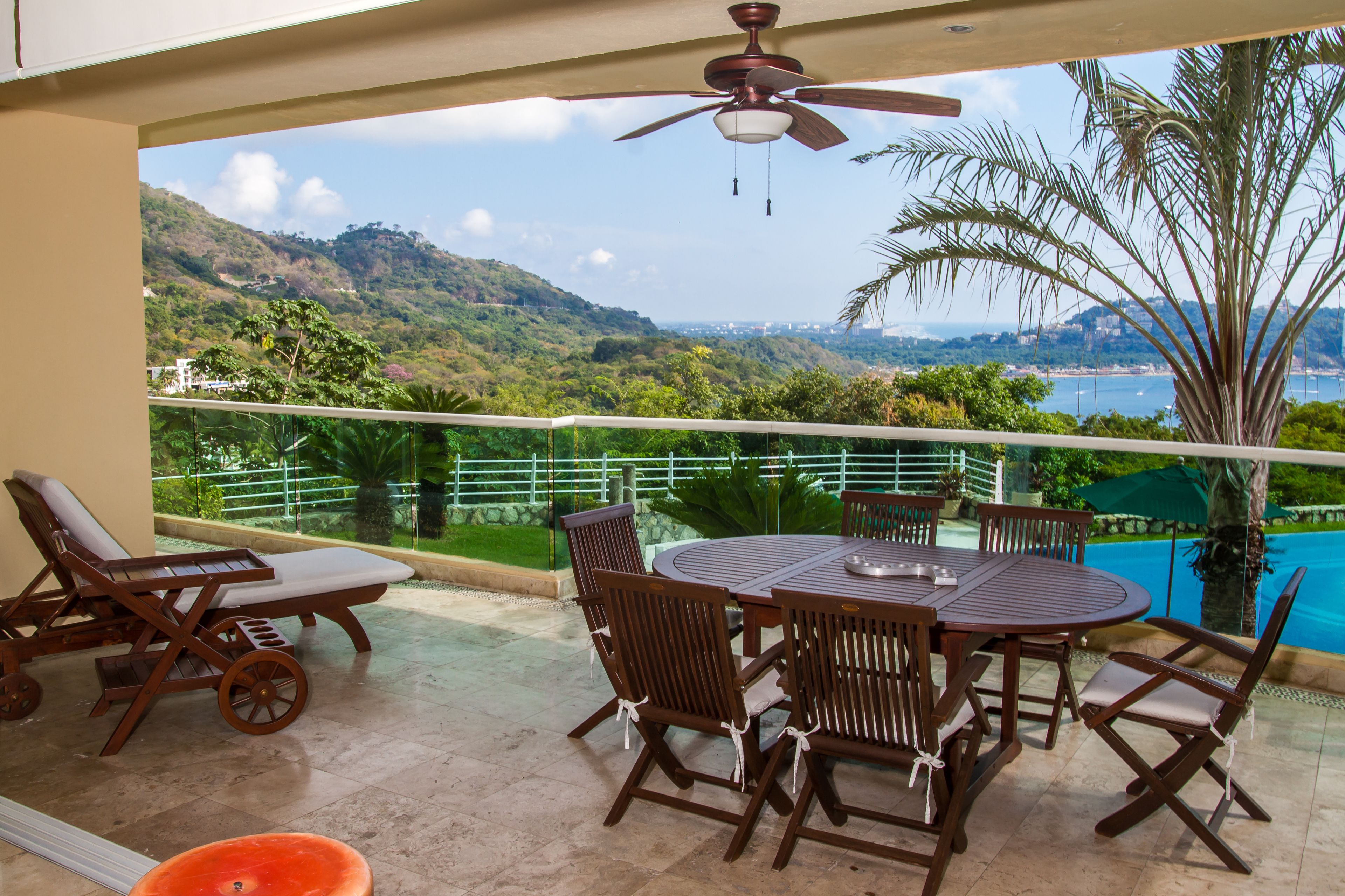 A balcony with a table and chairs, overlooking a scenic view of hills and a body of water.