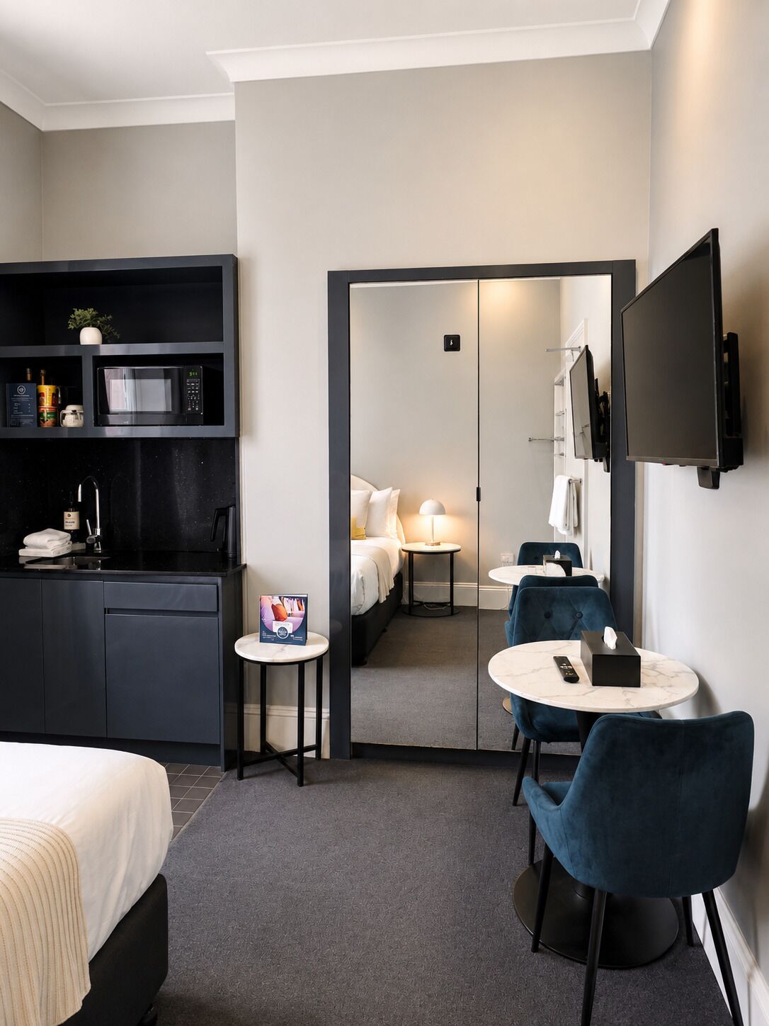 Habitación de hotel con cama, escritorio con computadora, mesita con control remoto, espejo y televisor montado en la pared.