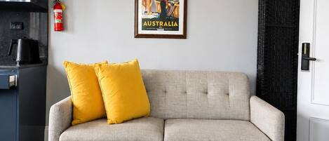 Ein Wohnzimmer mit einer Couch, einem Couchtisch, einem gerahmten Bild, einem Feuerlöscher und einer Küchenzeile.