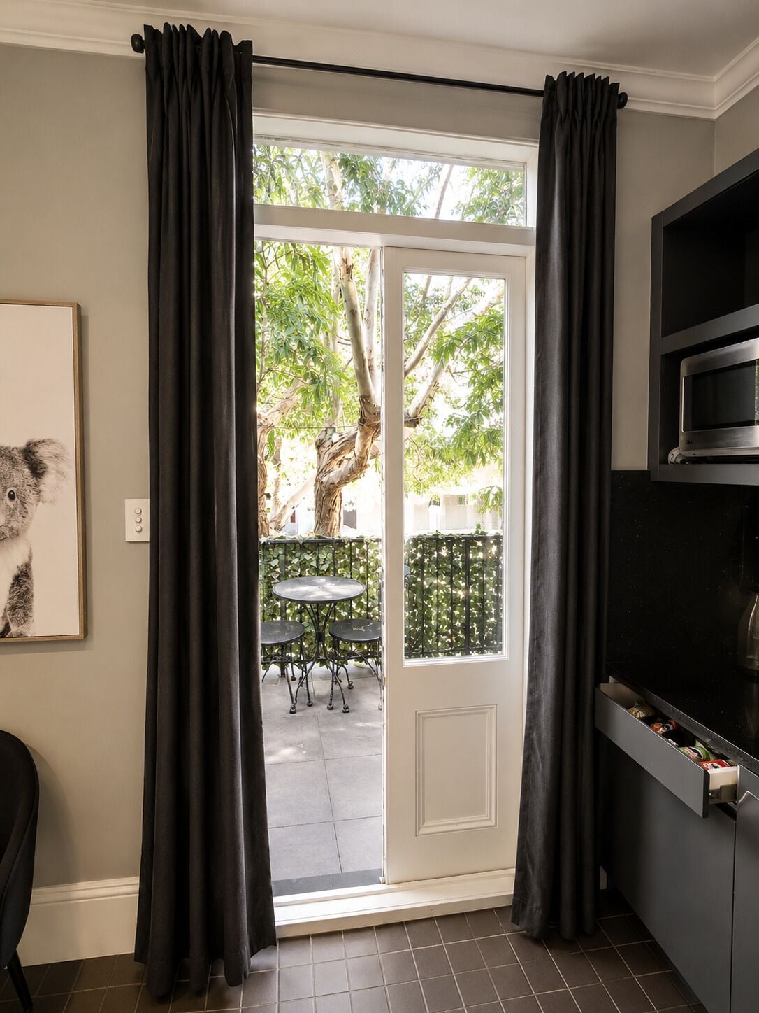 A kitchen with a microwave, a door leading to a patio with a table and chairs, and a framed picture on the wall.