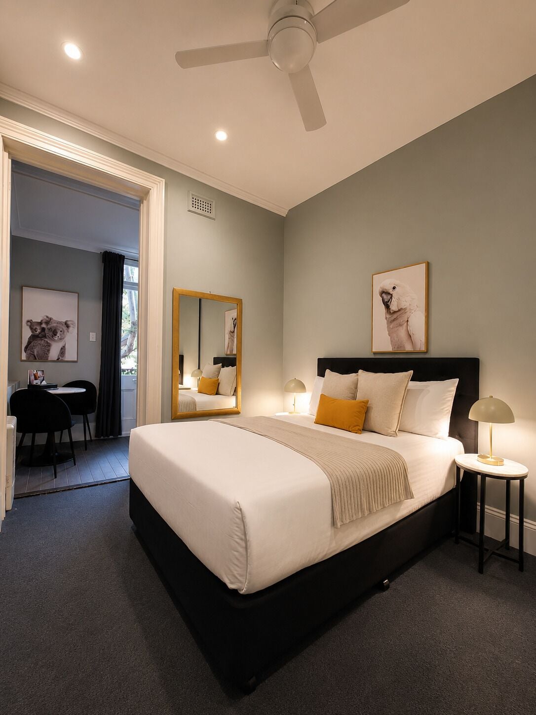 Un dormitorio con cama, mesitas de noche, ventilador de techo, espejo y obras de arte en las paredes.