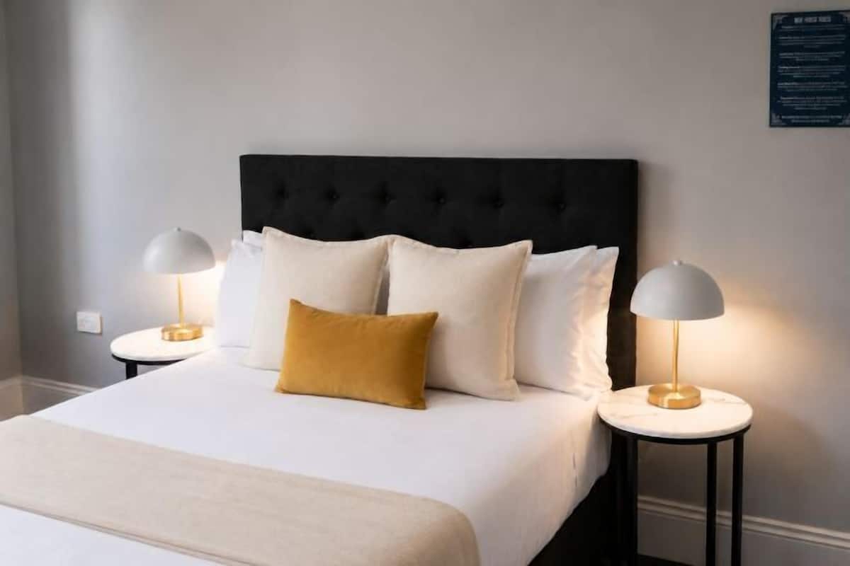 Une chambre d’hôtel avec un grand lit, deux tables de chevet avec des lampes et une tête de lit sombre.