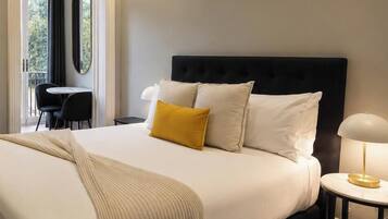 A bed with a dark headboard, white and yellow pillows, and a beige throw blanket.