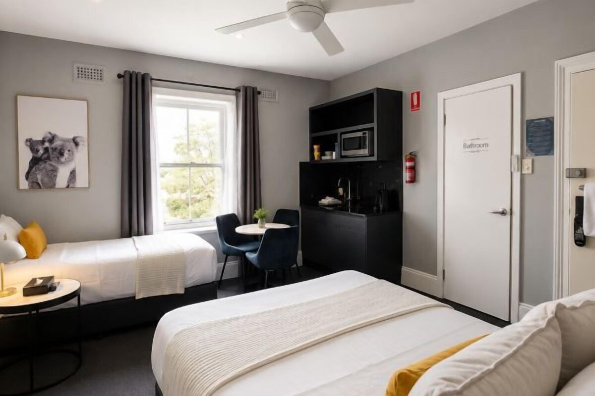 A hotel room with a bed, a desk, a chair, a microwave, and a door labeled 'Bathroom'.