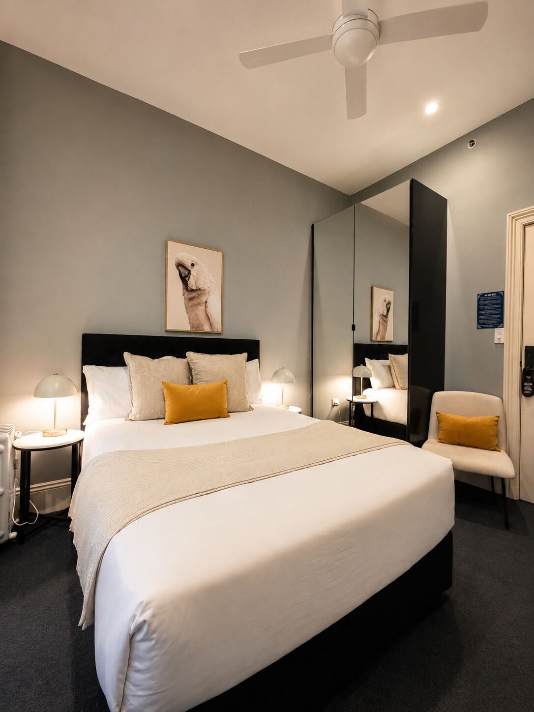 A modern hotel room with a large bed, a ceiling fan, a chair, and a mirror.