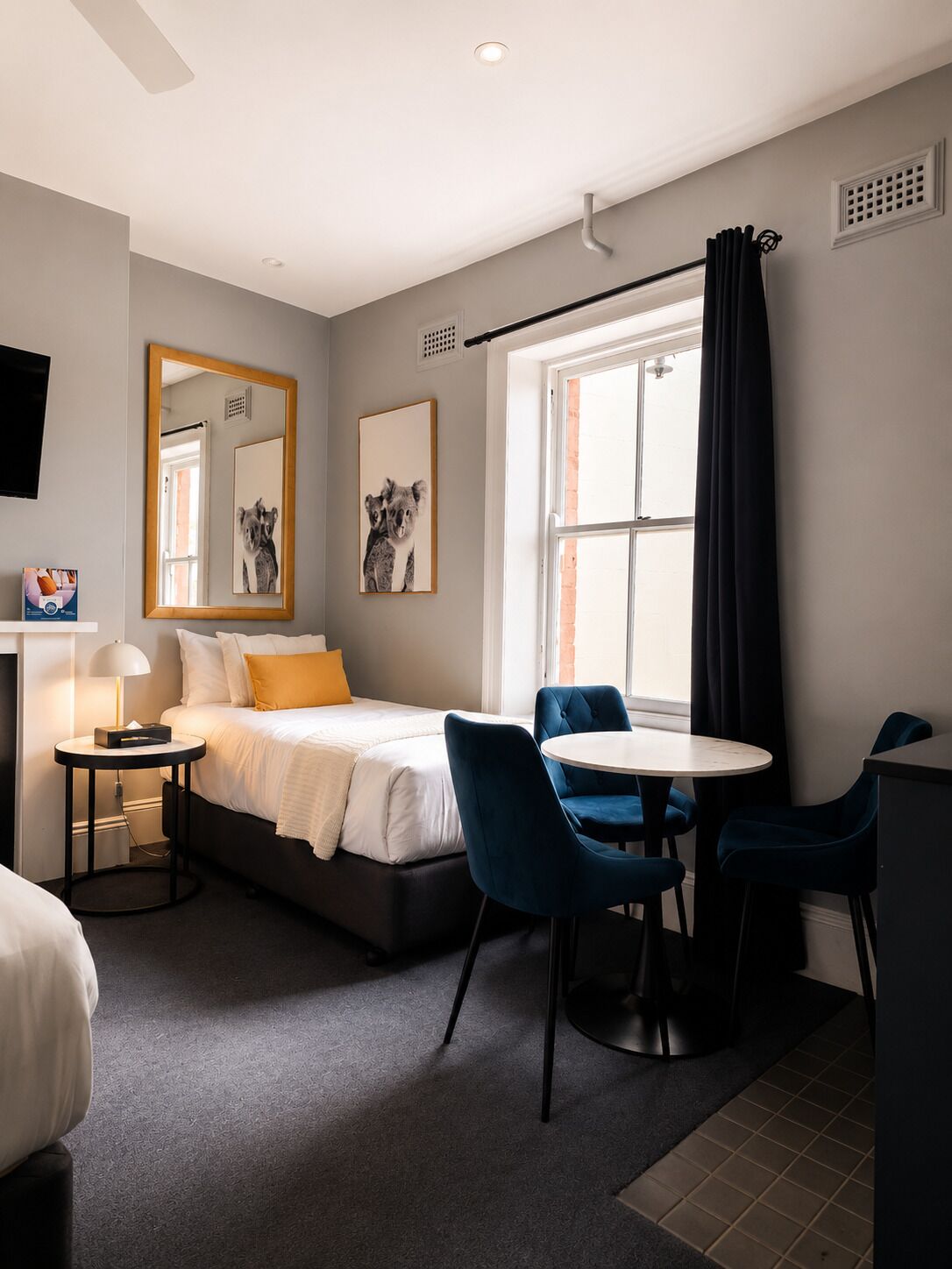Una moderna camera d'albergo con un letto, un tavolo rotondo, due sedie, una TV, uno specchio e opere d'arte.