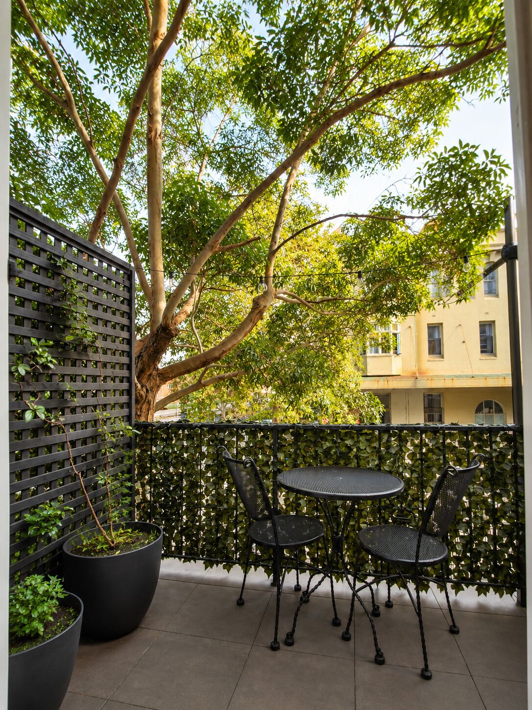 A balcony with a table and chairs, surrounded by a black metal fence and potted plants.