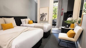 Habitación de hotel con dos camas, un pequeño rincón de estar, un cuadro en la pared y vistas al exterior.