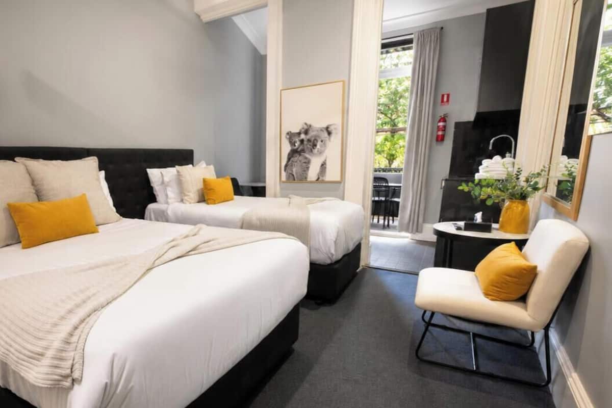 Une chambre d’hôtel avec deux lits, un petit coin salon, un tableau encadré au mur et une vue sur l’extérieur.