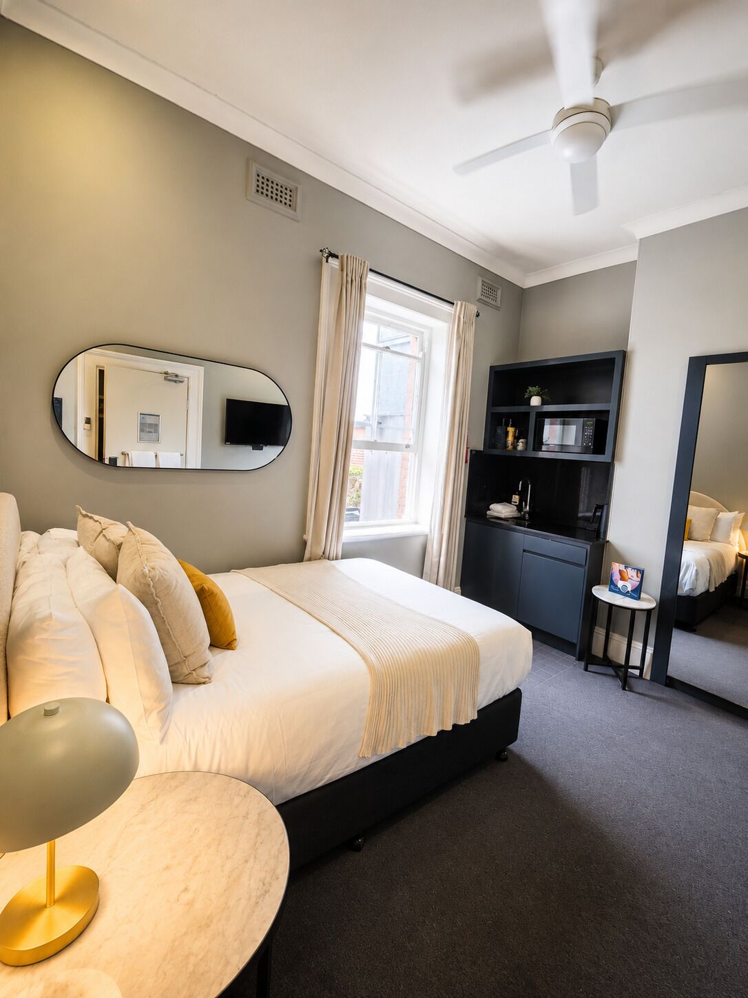 Habitación de hotel con cama, escritorio, silla, televisión, microondas y una pequeña mesa con una silla.