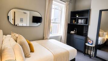Habitación de hotel con cama, escritorio, silla, televisión, microondas y una pequeña mesa con una silla.