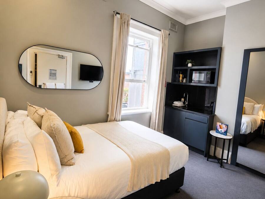 Habitación de hotel con cama, escritorio, silla, televisión, microondas y una pequeña mesa con una silla.