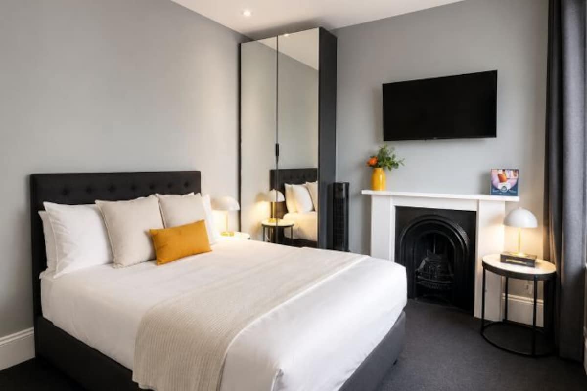 A hotel room with a large bed, a fireplace, a flat-screen TV, and a mirror.