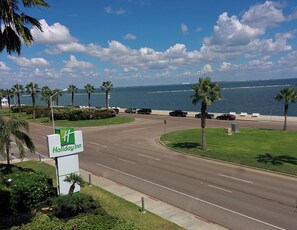 Een Holiday Inn bord, een weg met voertuigen, palmbomen en uitzicht op de oceaan.