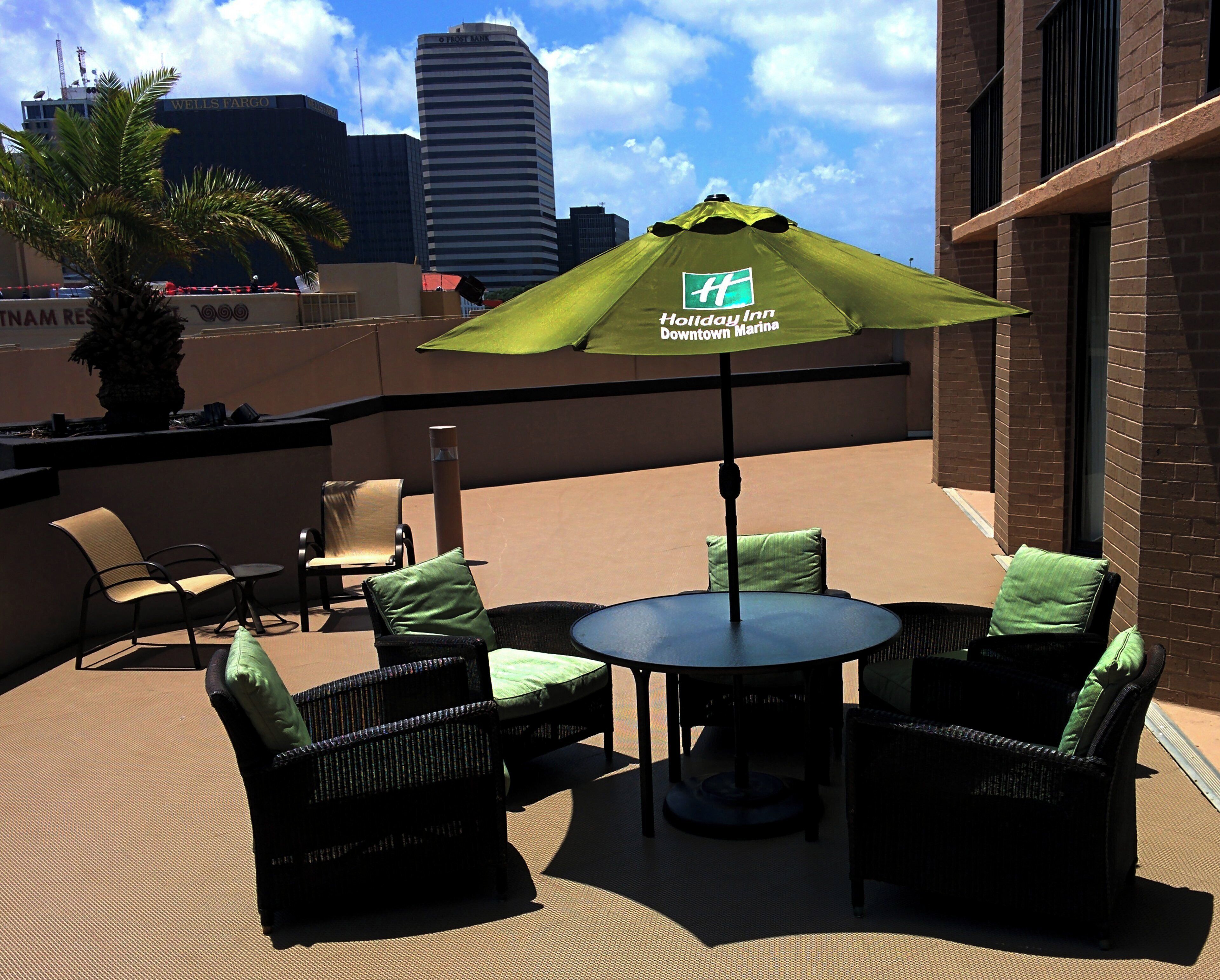 An outdoor seating area with wicker furniture and a green umbrella, overlooking a cityscape.