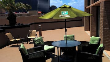 An outdoor seating area with wicker furniture and a green umbrella, overlooking a cityscape.