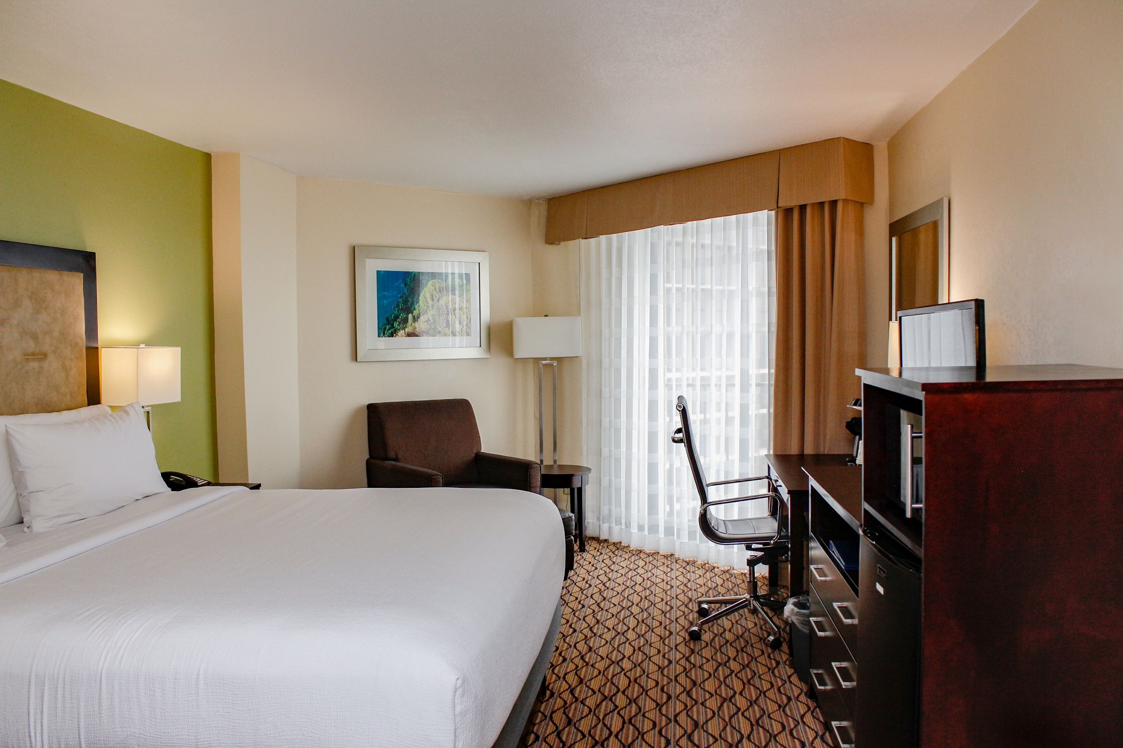 A hotel room with a large bed, a desk, a chair, a TV, and a painting on the wall.
