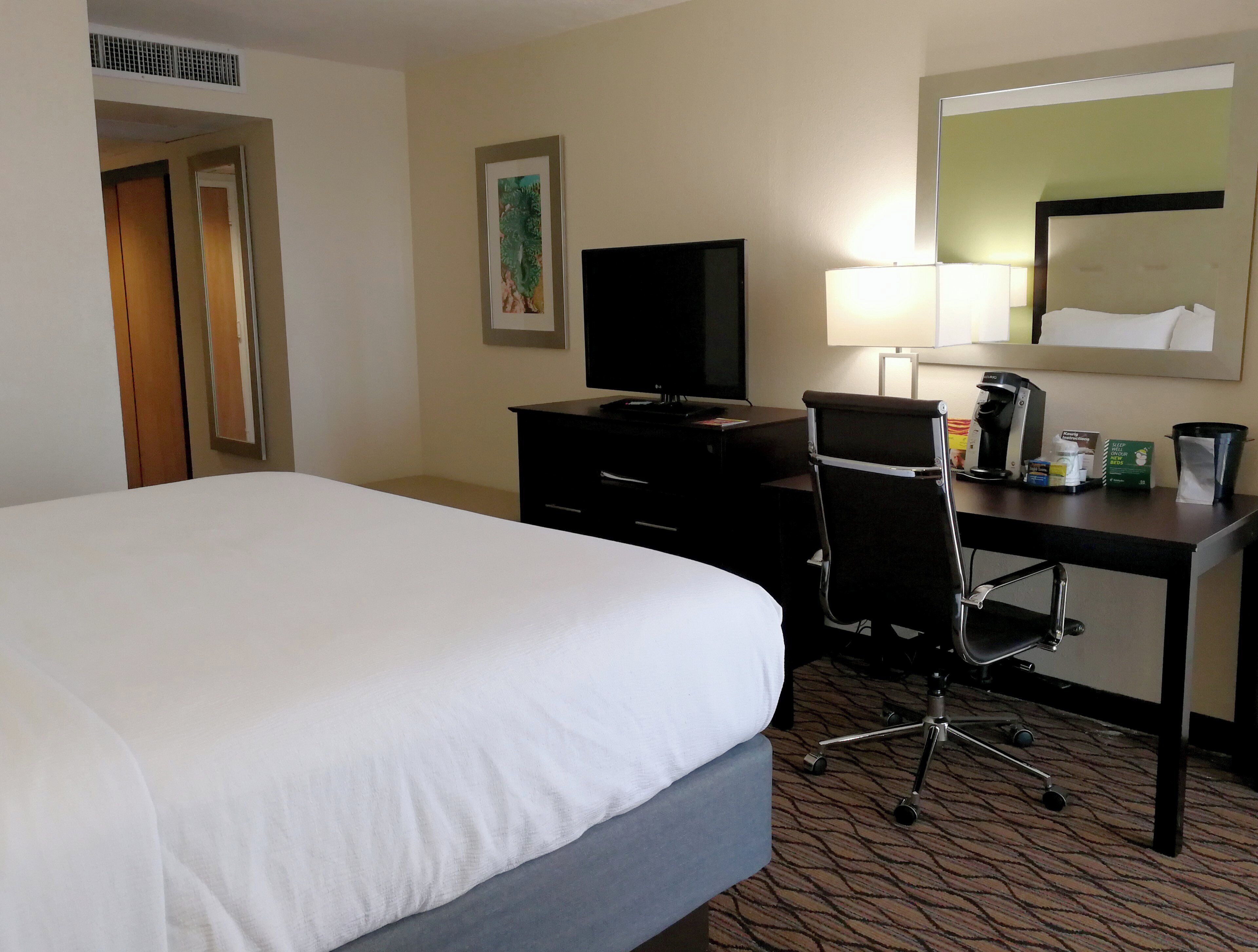 A hotel room with a bed, a desk with a chair, a television, a lamp, and a coffee maker.