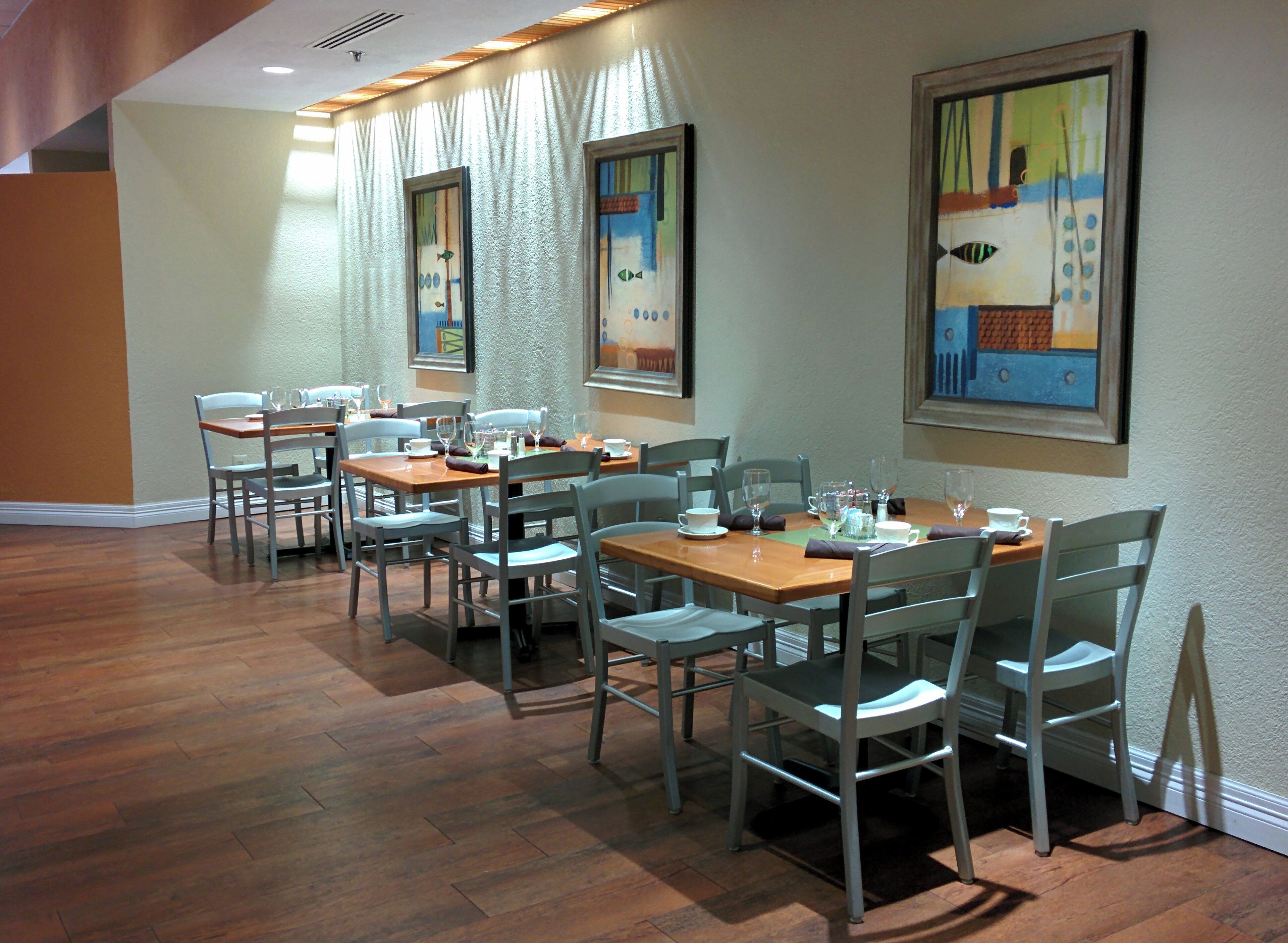 A dining area with multiple tables and chairs, wooden flooring, and framed artwork on the walls.