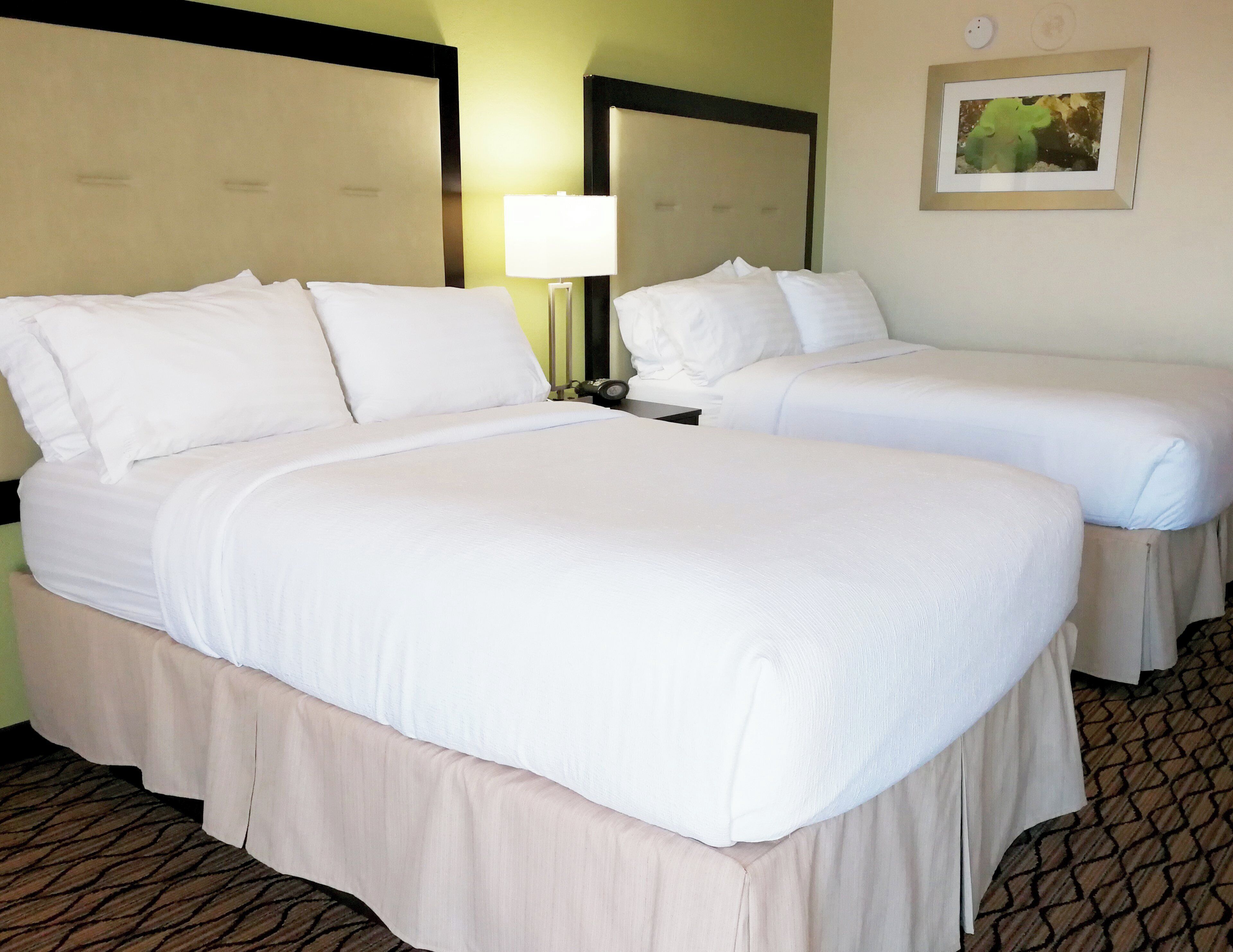 A hotel room with two beds, a nightstand, a lamp, and a framed picture on the wall.