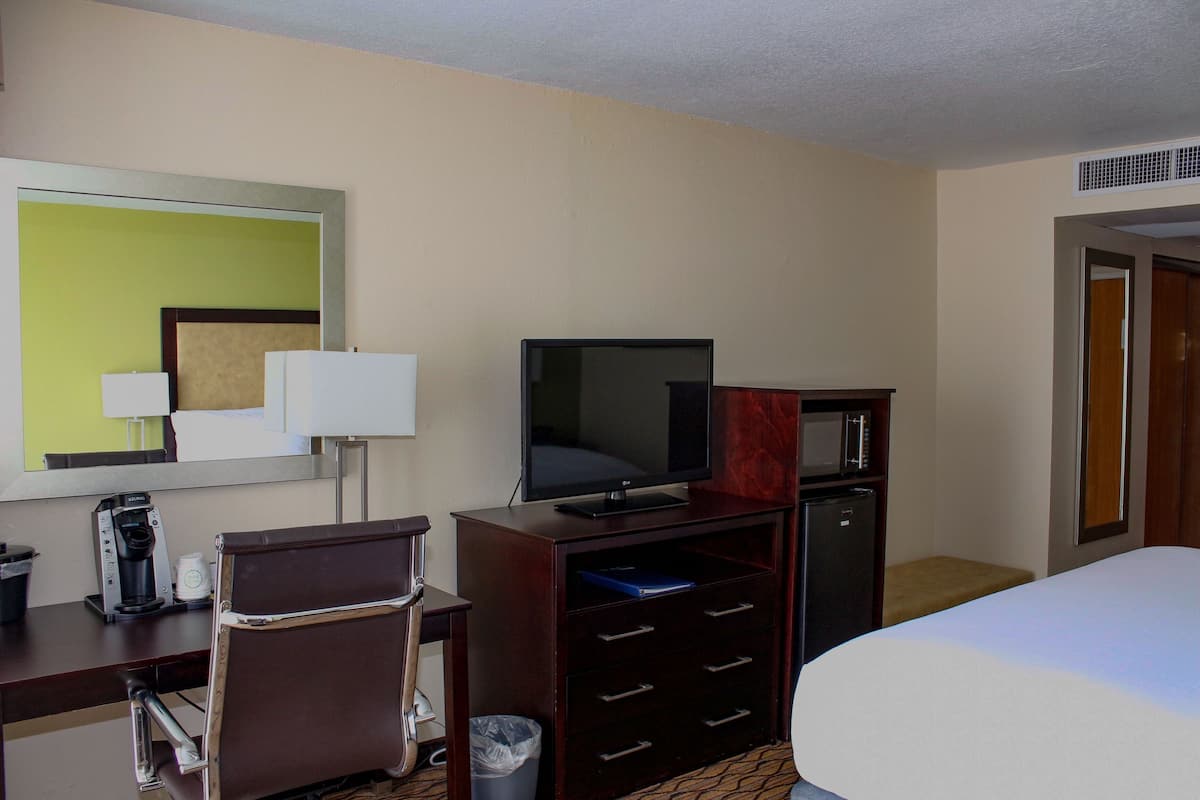 Ein Hotelzimmer mit Bett, Schreibtisch mit Stuhl, Fernseher, Mikrowelle und Mülleimer.