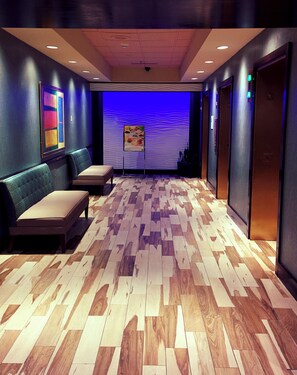Un hall d’hôtel doté d’un sol en bois à motifs, d’un espace détente avec des bancs et d’un mur agrémenté d’un panneau lumineux bleu.