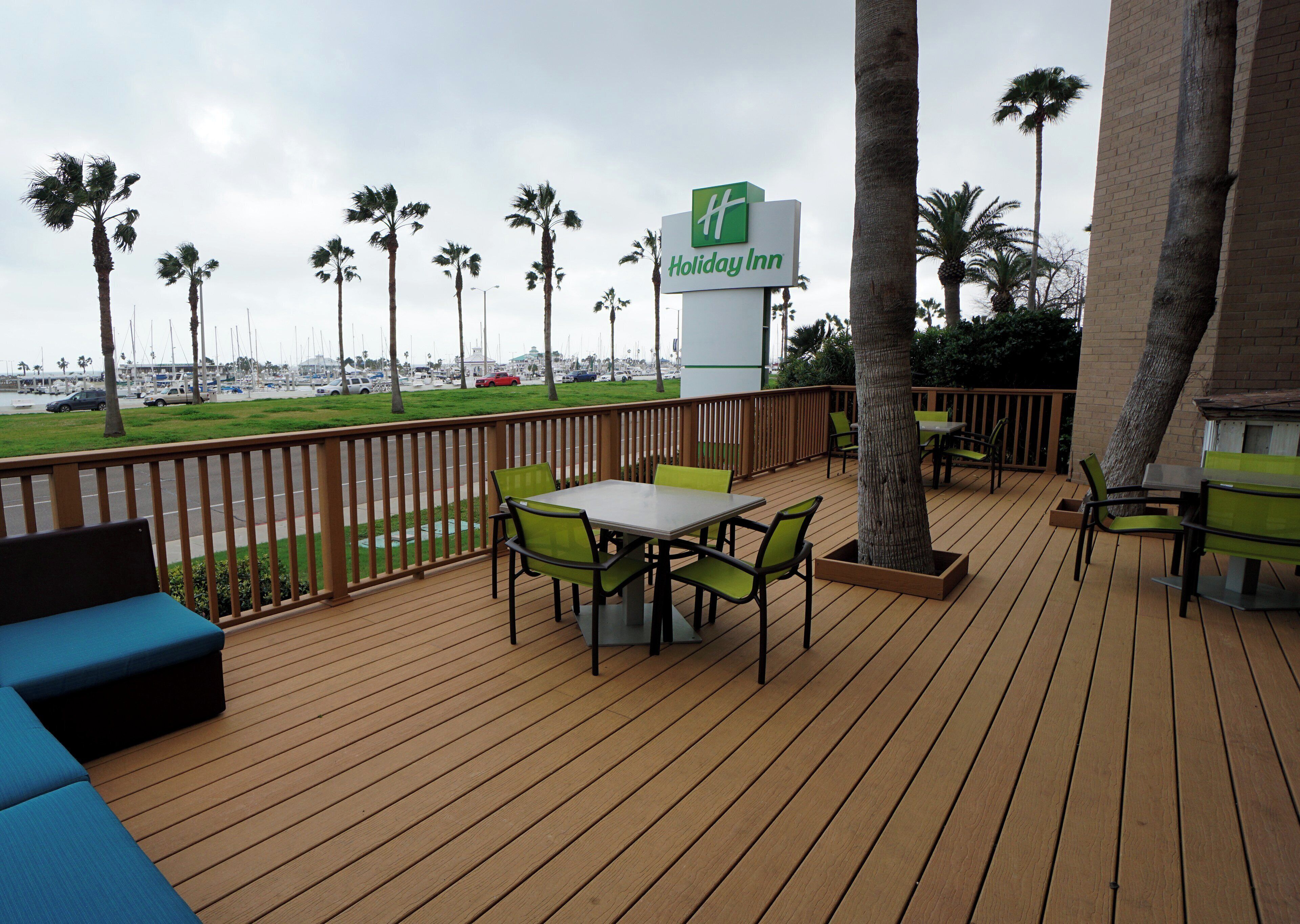 Eine Holzterrasse mit Sitzgelegenheiten im Freien, einem Schild für Holiday Inn und Palmen im Hintergrund.