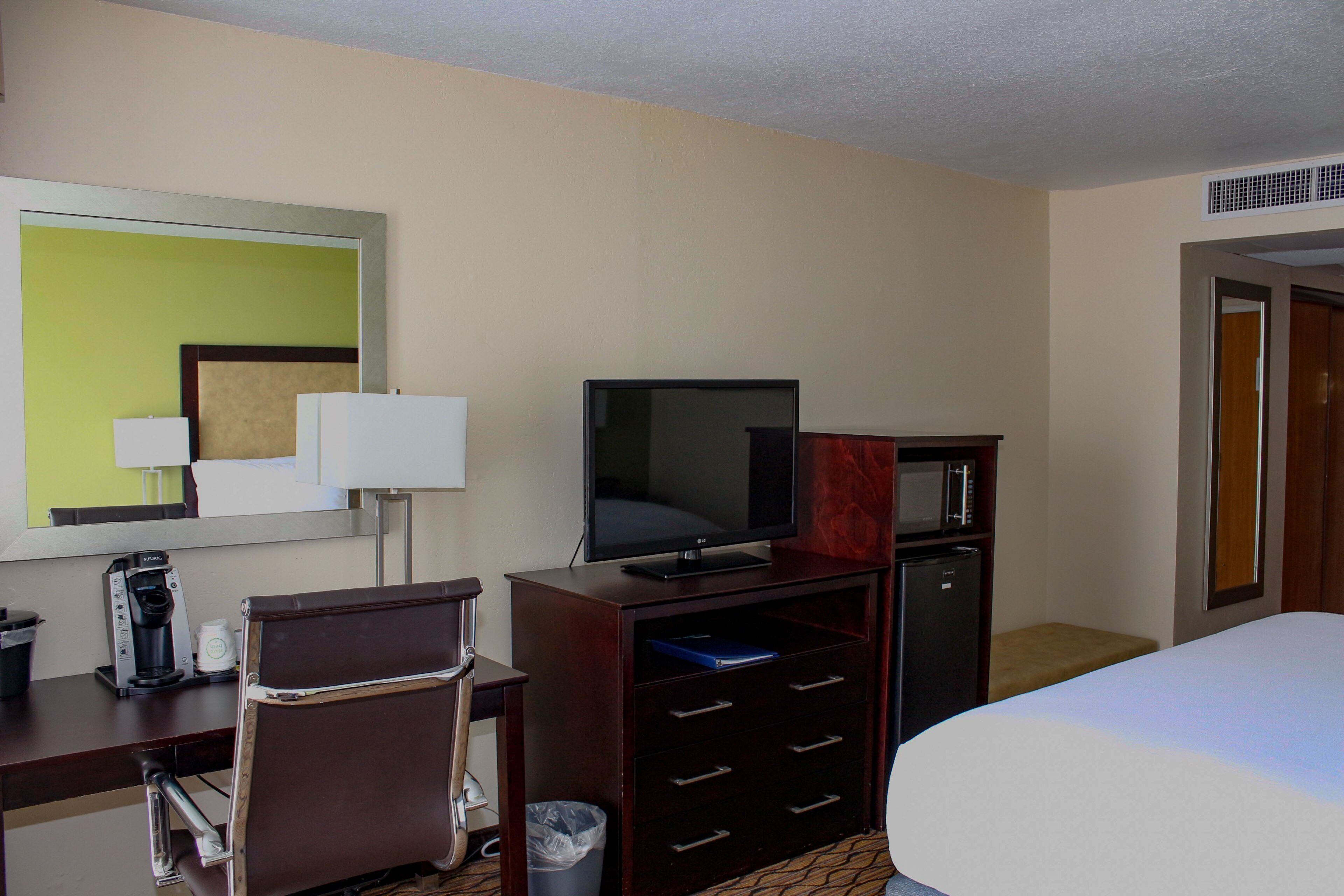 A hotel room with a bed, a desk with a chair, a television, a microwave, and a trash can.