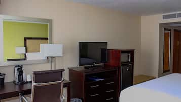 A hotel room with a bed, a desk with a chair, a television, a microwave, and a trash can.