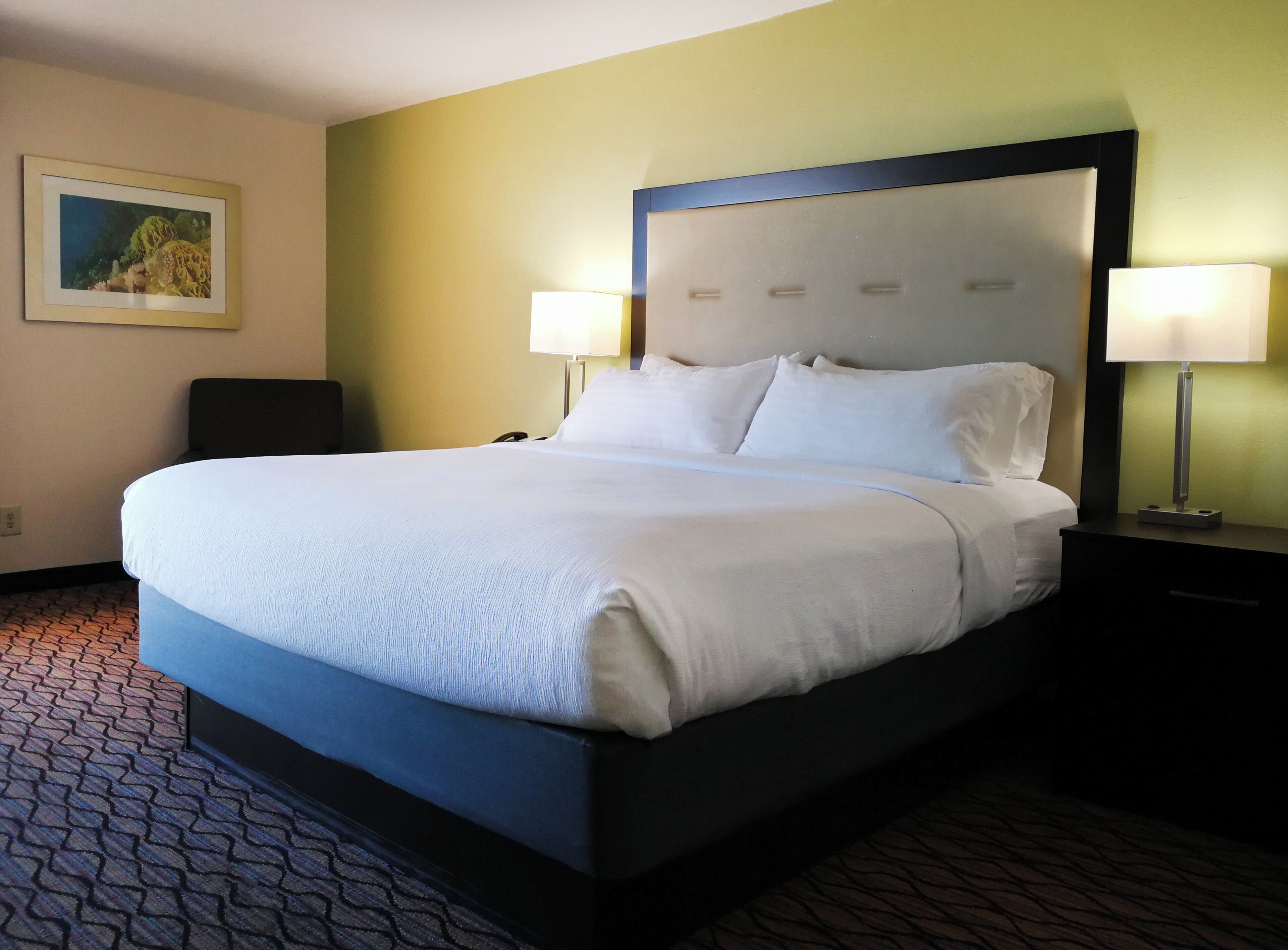 A hotel room with a large bed, two bedside lamps, a headboard, and a painting on the wall.
