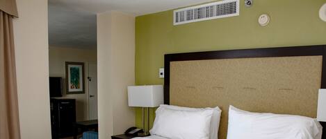 A hotel room with a large bed, a bedside table with a lamp, a phone, and a painting on the wall.
