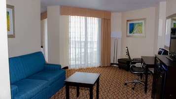 Ein Hotelzimmer mit einem blauen Sofa, einem kleinen Tisch, einem Schreibtisch mit Stuhl, einem Fernseher und einem Bild an der Wand.