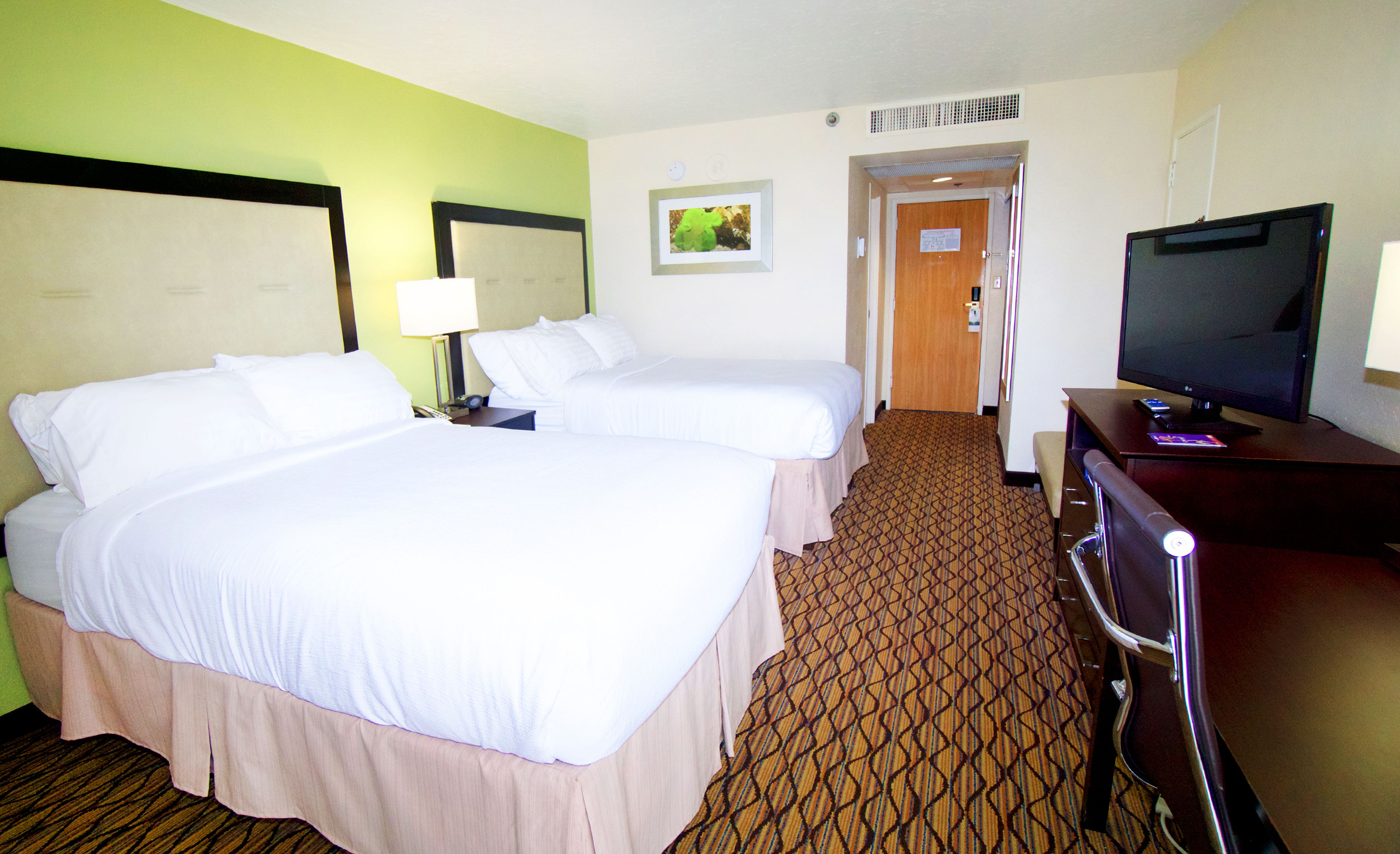 A hotel room with two beds, a television, and a desk.