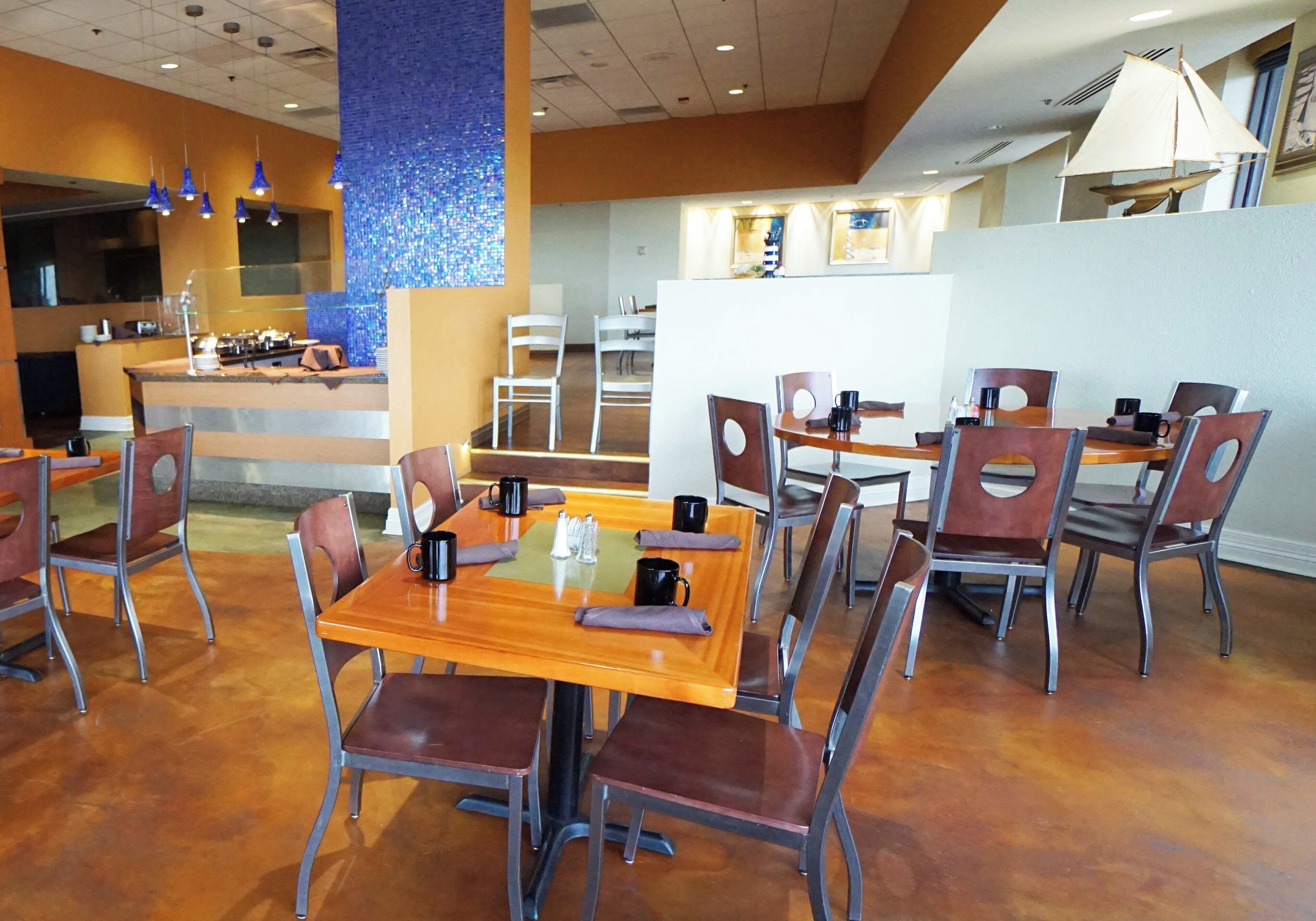 A restaurant with multiple tables and chairs, a kitchen area, and a decorative blue wall.