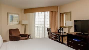 A hotel room with a bed, a desk with a chair, a television, a lamp, and a window with curtains.